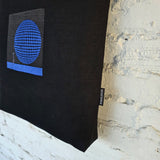 Blue circular 3D embroidered design on black tote bag, modern geometric textile art detail