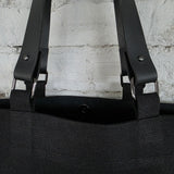 Close-up of a black linen-cotton tote bag showing the removable genuine leather handles, metal rings, and sturdy stitching, highlighting quality