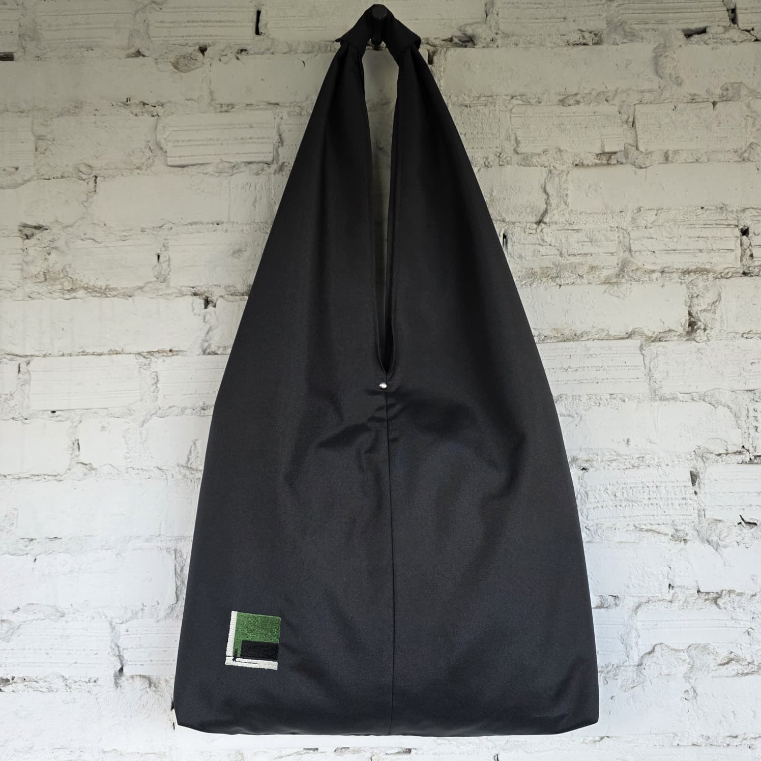 Black bag with a small green label on a white brick wall background