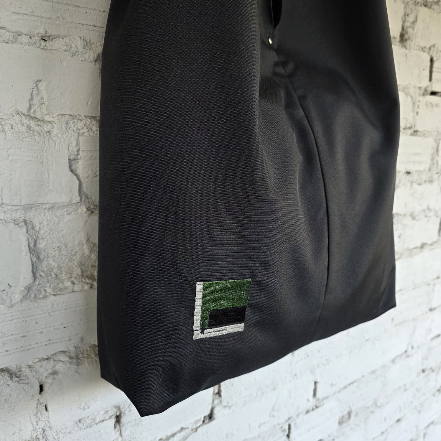 Black bag with a green and gray label against a textured white brick wall.