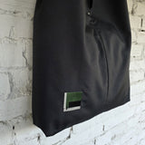 Black bag with a green and gray label against a textured white brick wall.