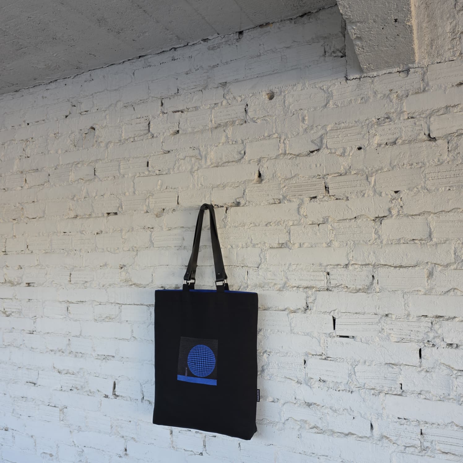 Side view of structured black embroidered tote bag with detachable leather handles, contemporary art-inspired handbag