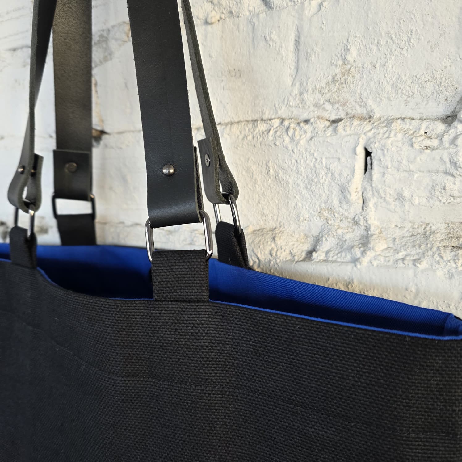 Black canvas tote bag with detachable genuine leather handles and blue lining detail, close-up of durable metal hardware and minimalist handmade construction