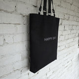 Black linen-cotton tote bag with removable leather handles, embroidered “Happy Day” text, minimalist everyday design