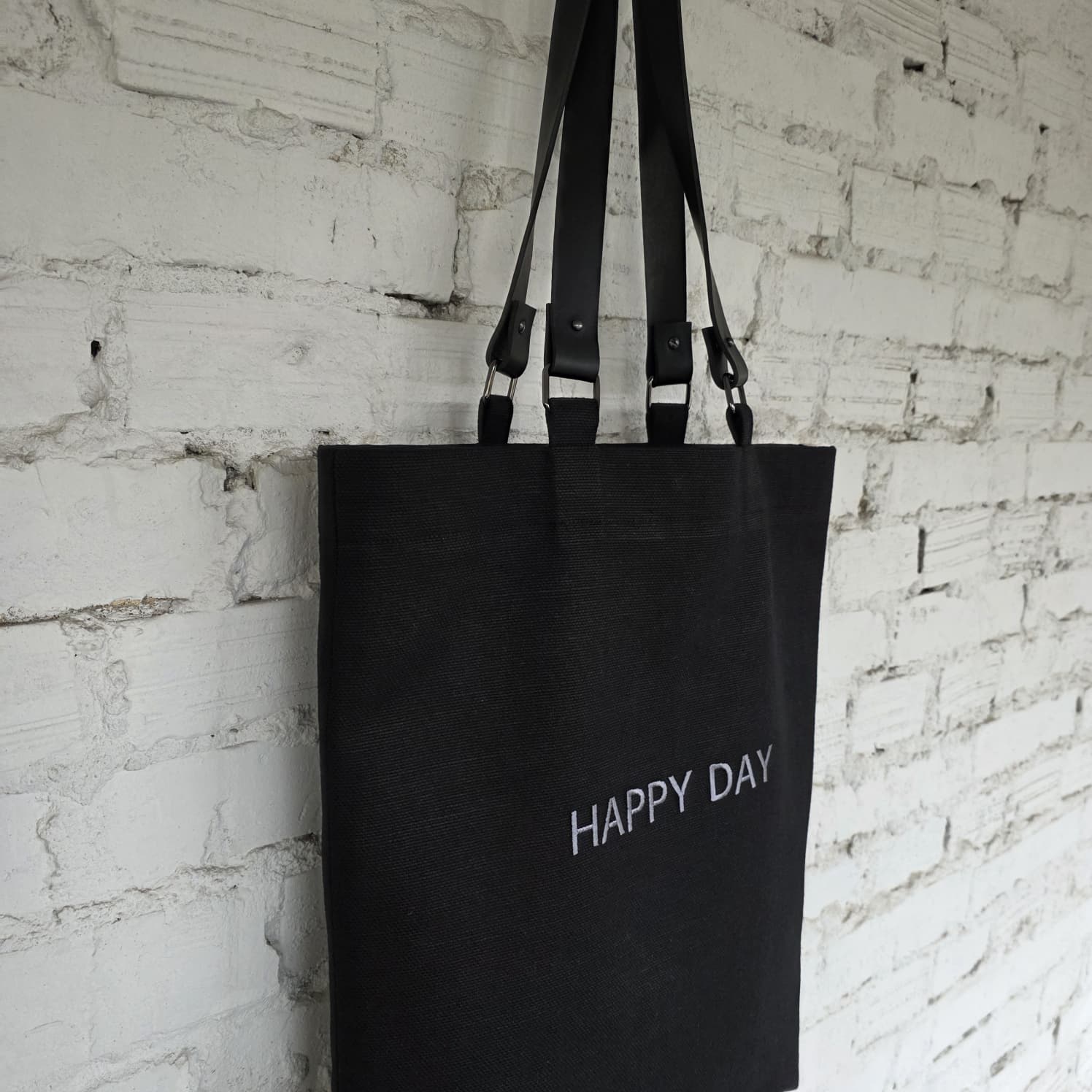 Large black linen-cotton tote with removable leather handles displayed against a light wall, minimalist and durable everyday bag