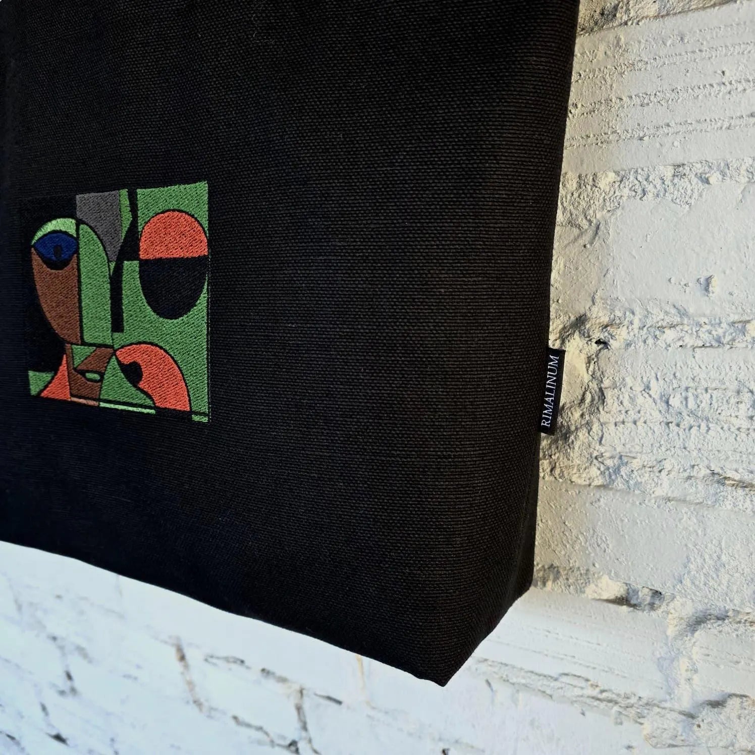 Black bag with colorful geometric design and brand tag on a textured surface