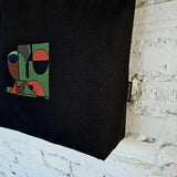 Black bag with colorful geometric design and brand tag on a textured surface