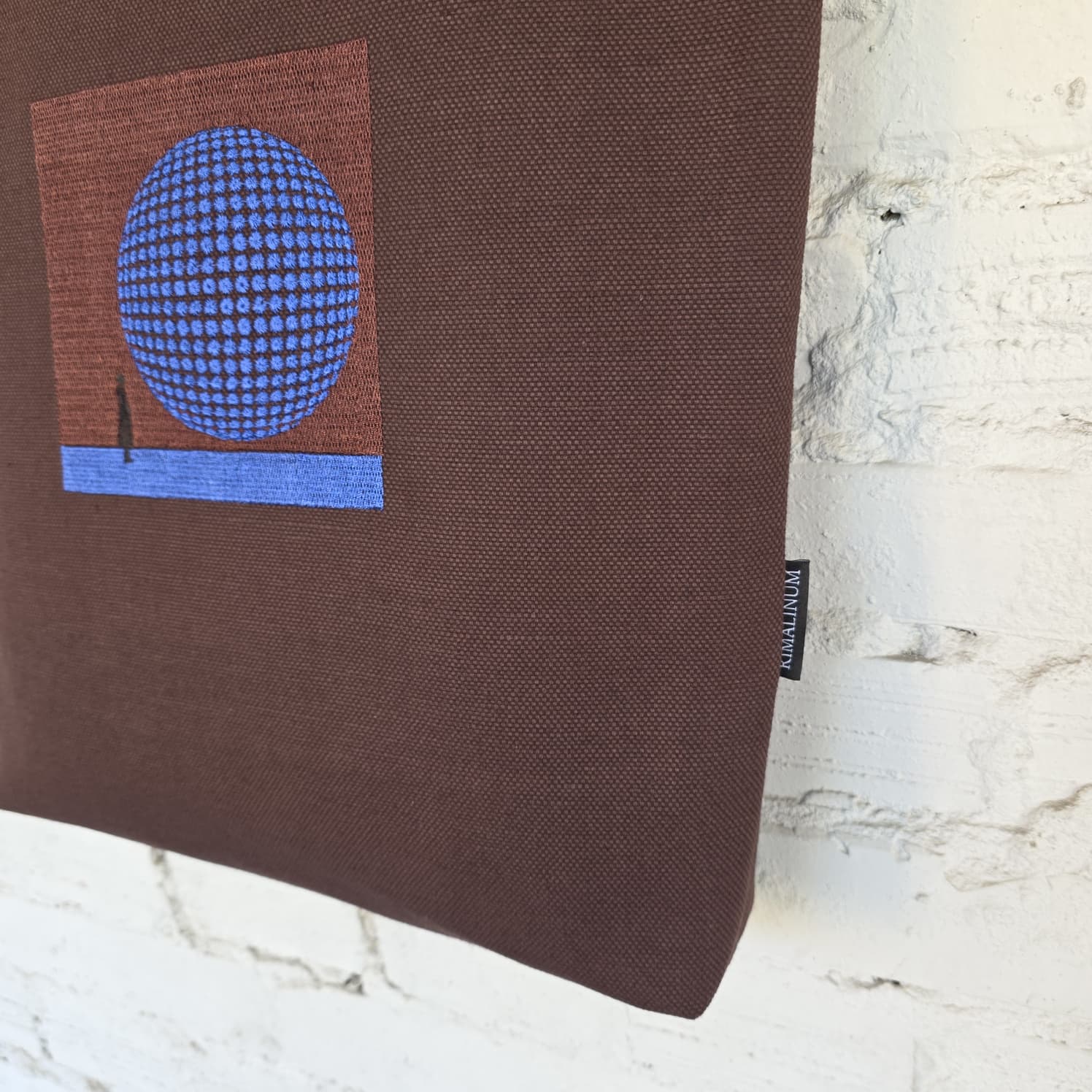 Close-up of cobalt blue 3D-effect circular embroidery on textured brown tote bag fabric, showing the intricate geometric pattern.