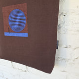 Close-up of cobalt blue 3D-effect circular embroidery on textured brown tote bag fabric, showing the intricate geometric pattern.