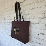 Brown tote bag with abstract design hanging against a white brick wall
