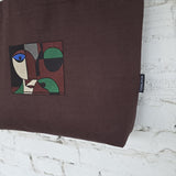 Handmade brown tote bag with detachable leather handles and green lining shown from side angle