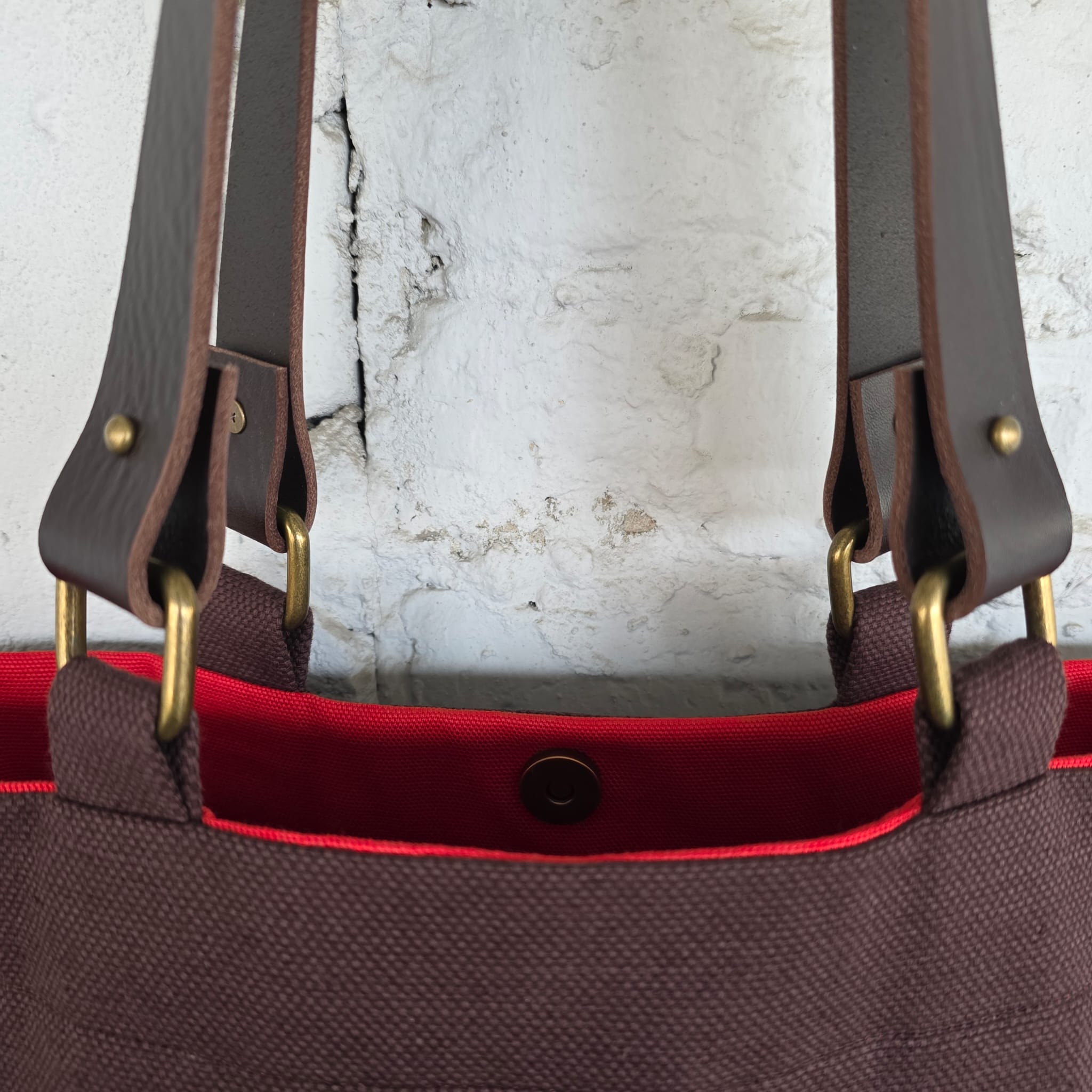 Close-up of brown tote bag with detachable leather handles and brass hardware details