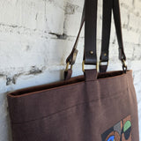 Brown tote bag with decorative design on a textured white wall background