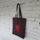 Brown minimalist tote bag with red geometric embroidery hanging against textured wall