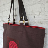 Brown tote bag with red interior and pocket against a textured white wall