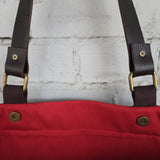 Red bag with brown straps and gold buckles against a textured white wall.