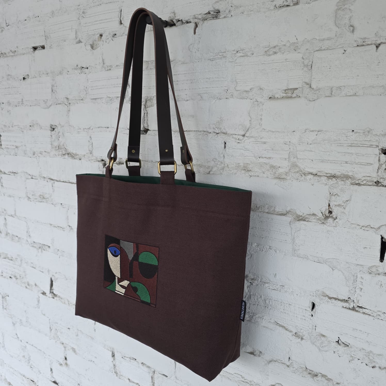 Brown tote bag with a colorful design on a white brick wall