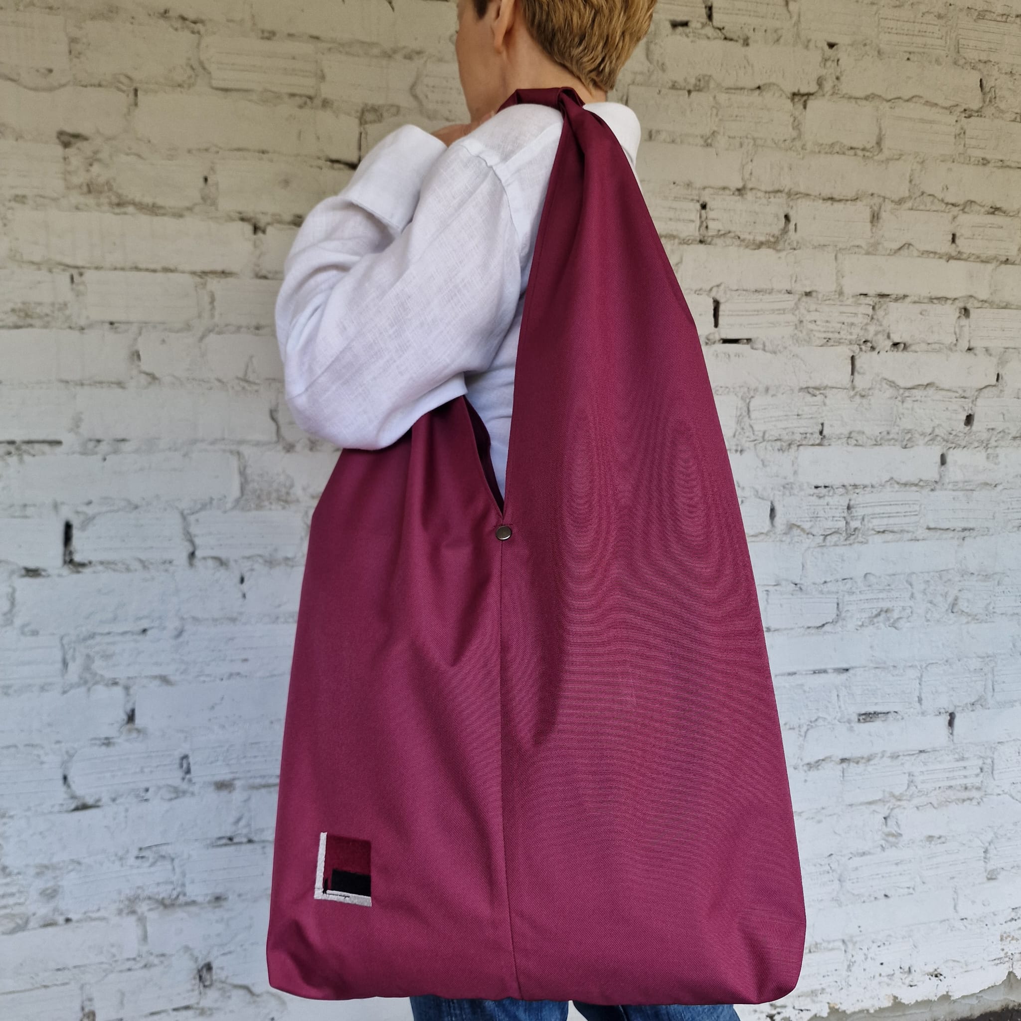 Burgundy waterproof hobo bag worn on shoulder, large minimalist fabric bag in deep wine red color, lightweight everyday women’s bag