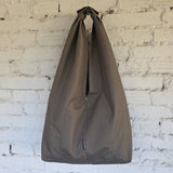 A large khaki waterproof hobo bag with a top loop, hanging against a white brick wall.