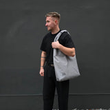 Man holding a gray tote bag against a dark background