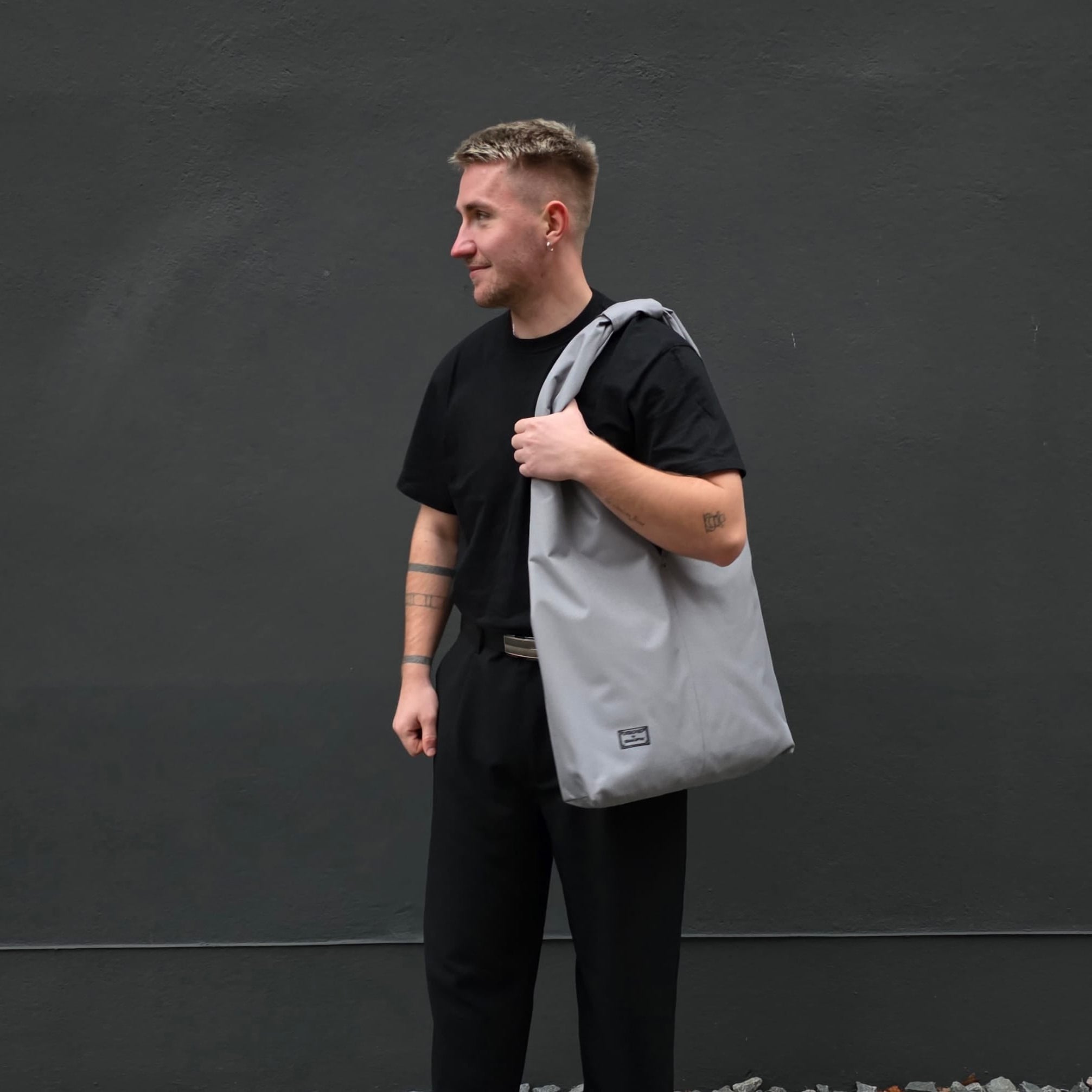 Man holding a gray tote bag against a dark background