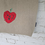 A beige linen tote bag with a red poppy cluster embroidered on the front, shown against a white brick wall background.