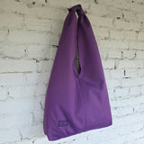 Oversized purple hobo shoulder bag hanging against a white brick wall, showing its soft slouchy silhouette.