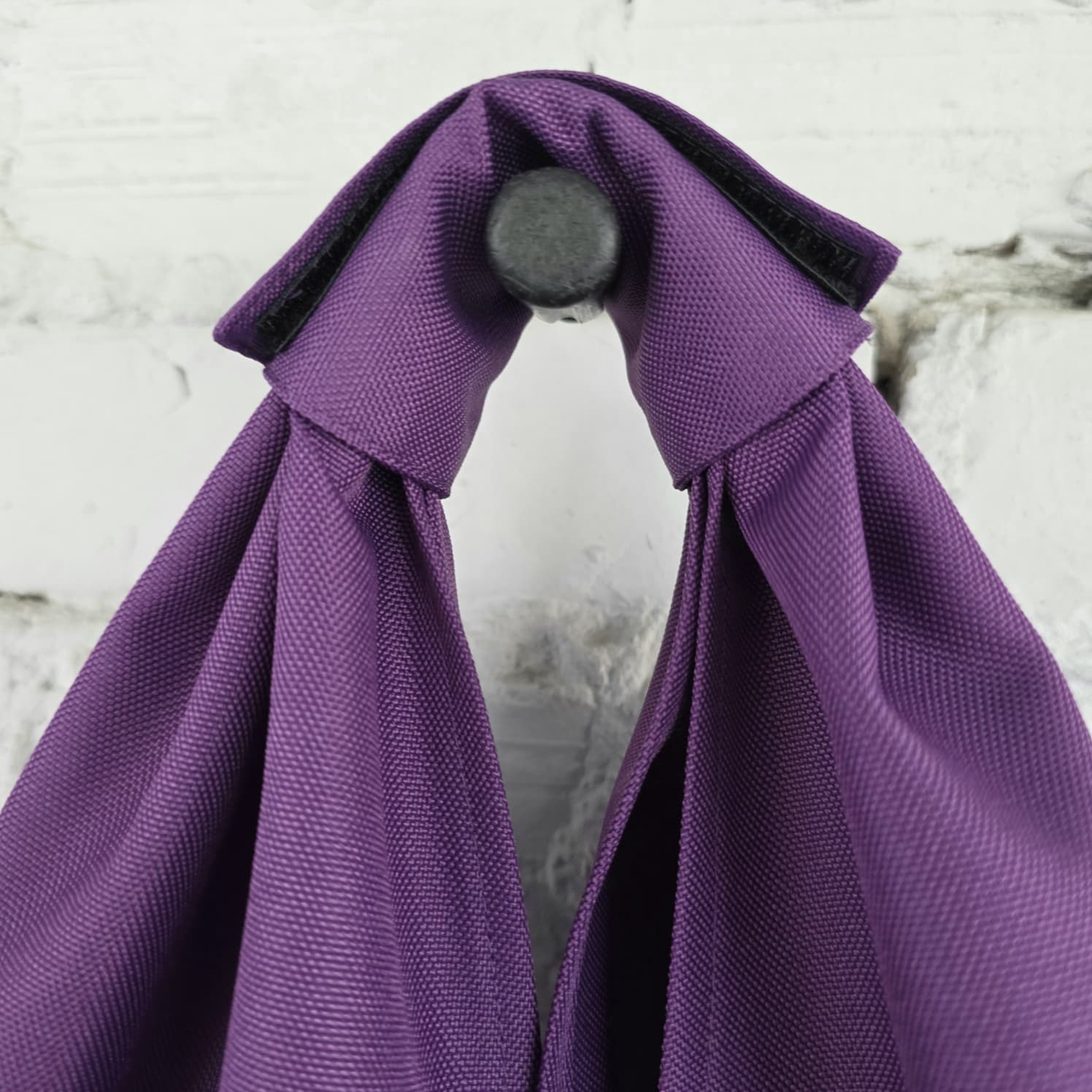 Close-up of purple hobo bag with wide integrated shoulder handle, woven fabric texture and black fastening detail.