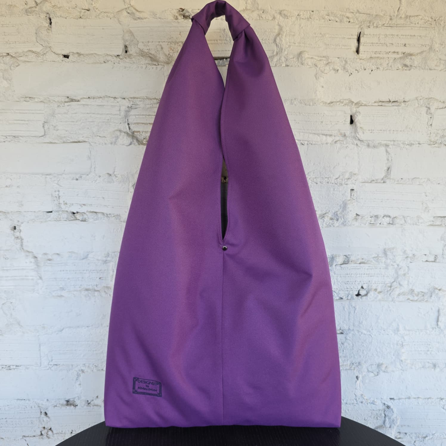 Large purple hobo bag displayed against a white brick wall, featuring a relaxed oversized shape and wide handle.