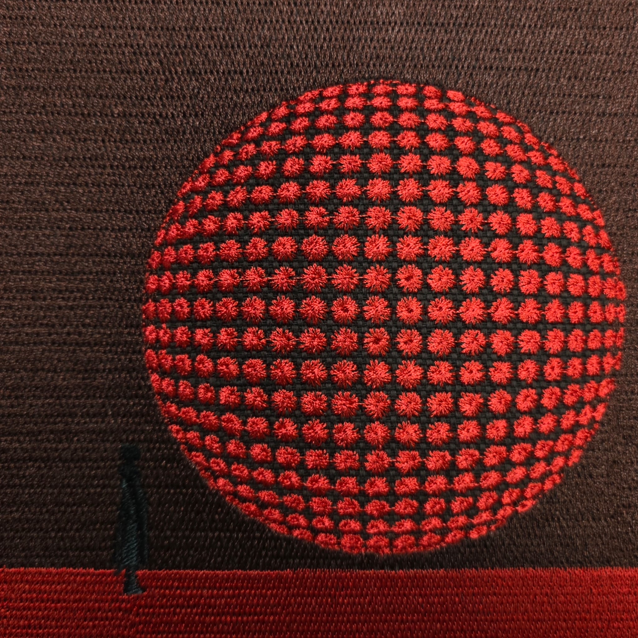 Detailed close-up of red 3D embroidered circle design on brown fabric tote bag
