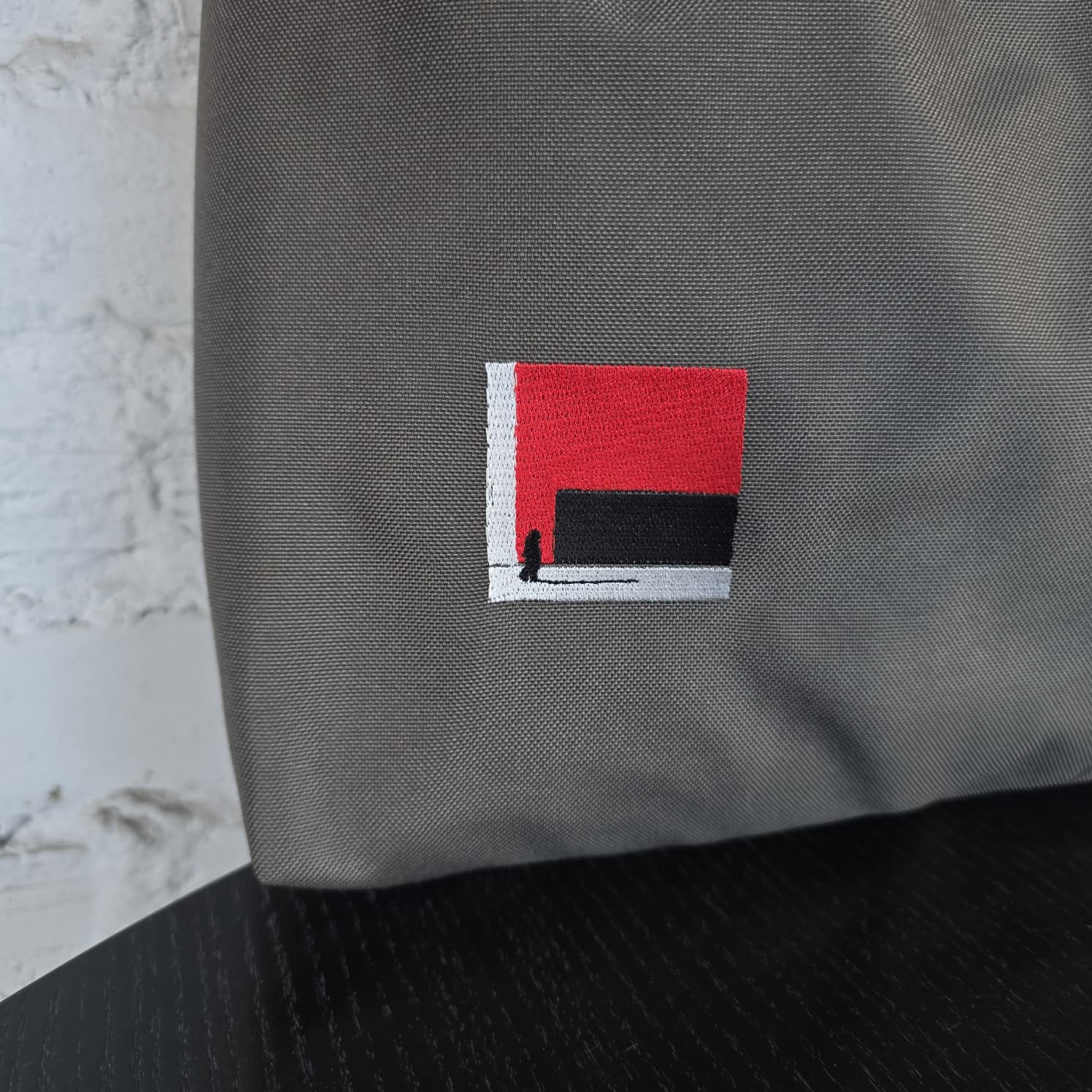 Red, black and grey geometric embroidery detail on khaki grey fabric