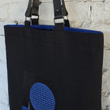 Modern black canvas tote bag with blue geometric embroidery and leather straps, structured minimalist shoulder bag