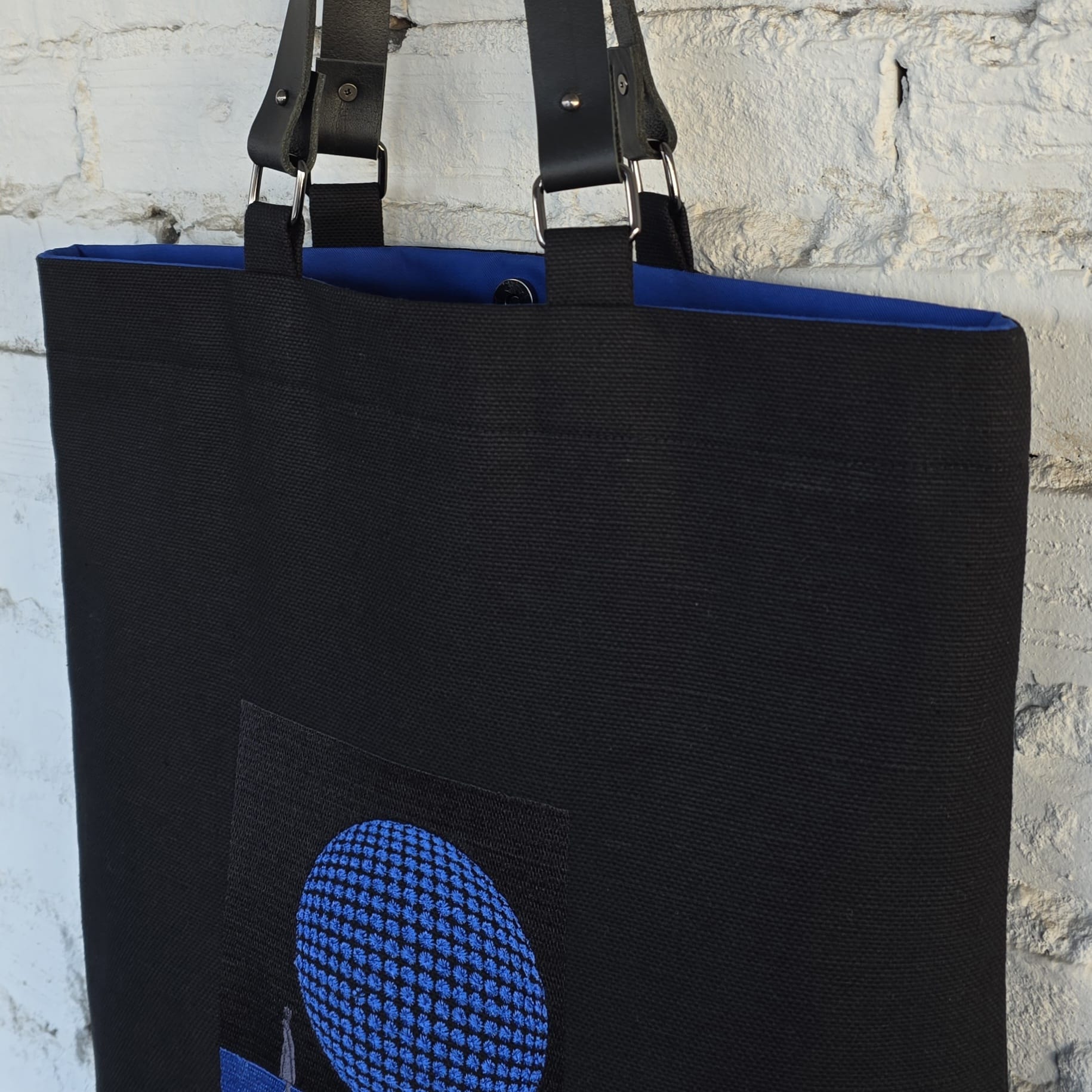 Modern black canvas tote bag with blue geometric embroidery and leather straps, structured minimalist shoulder bag