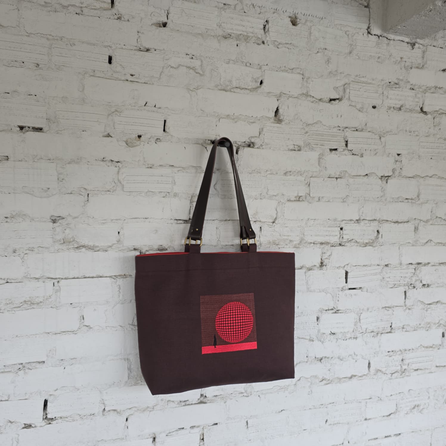 Brown tote bag with a red design on a white brick wall