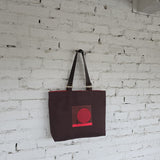 Brown tote bag with a red design on a white brick wall