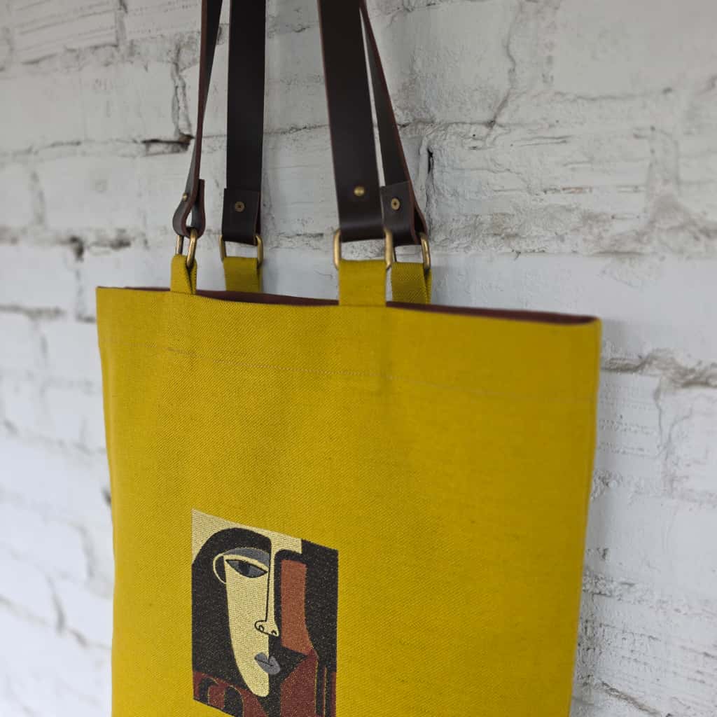 Yellow tote bag with artistic design on a white brick wall background