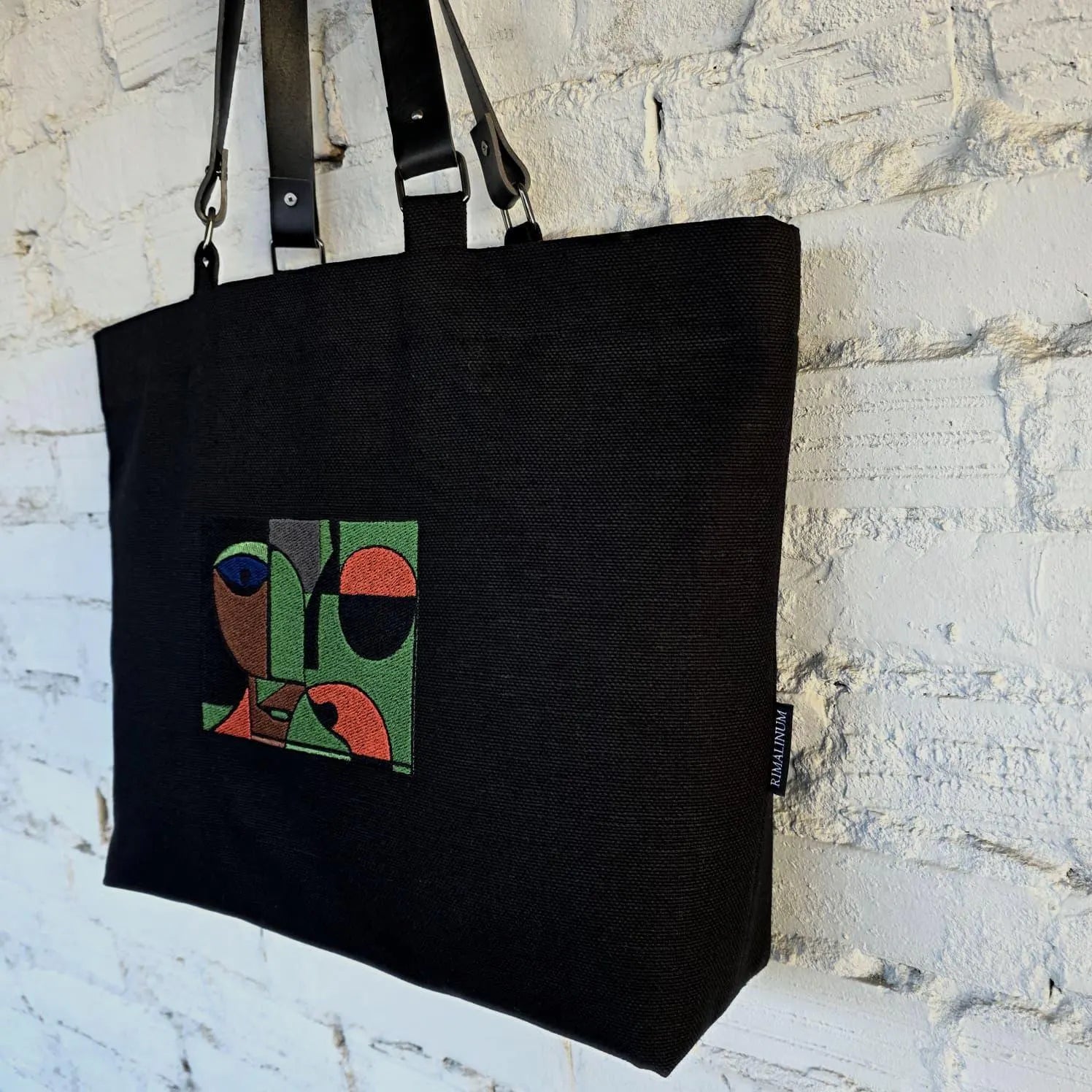Black handmade tote bag with embroidered abstract face design and detachable leather handles